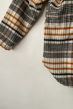 نمای نزدیک از آستین و لبه‌ی پایین کت چهارخونه زنانه به رنگ قهوه‌ای، بژ و مشکی با طراحی حلالی شکل