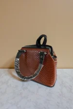 کیف دستی زنانه چرم قهوه‌ای با طرح موج‌دار و دسته‌های مشکی، نمای سه‌رخ از سمت راست روی سطح مرمر سفید با پس‌زمینه بژ